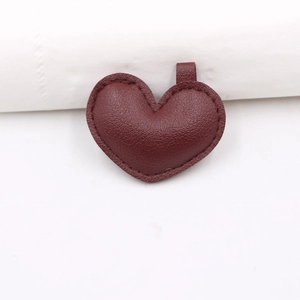 Dettaglio di ciondolo a cuore in pelle bordeaux con trama litchi e cuciture rifinite