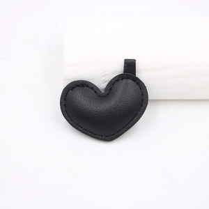 Dettaglio di un ciondolo a cuore in pelle nera con trama a grana e cuciture su sfondo bianco