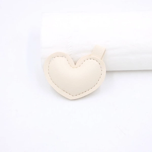 Vista dettagliata di un accessorio a cuore in pelle beige con cuciture e un passante per appendere