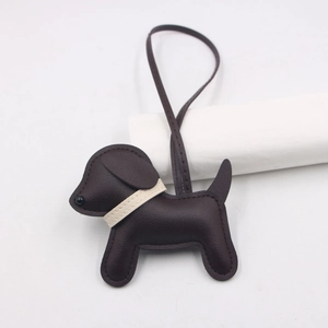 Close-up of a brown leather puppy bag charm with white stitching and a long strap