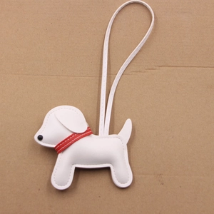 Close-up of white leather puppy charm with red collar on cardboard background