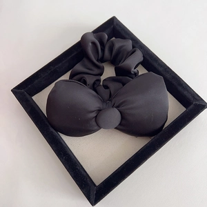 Detail of a large matte black bow scrunchie made of premium satin fabric on velvet