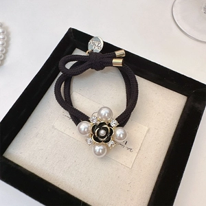 Close-up of elegant black camellia hair tie with pearls and gold charm on white card