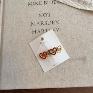 Elegant gold-plated hair clip featuring three decorative red and gold hearts on a card