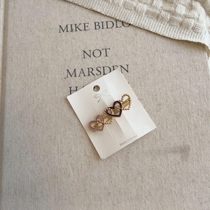 Elegant gold metal hair clip with three purple and hollow heart charms on a white card