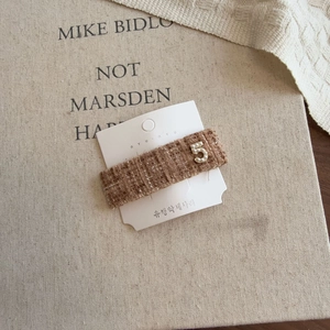 Detail of a brown tweed bow hair clip with faux pearl number five on a display card