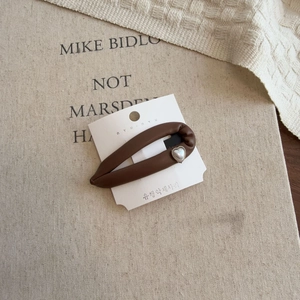 Detail of dark brown leather hair clip with heart pearl ornament on display card