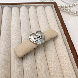 Beige faux leather hair clip with heart-shaped silver metal accent on display box