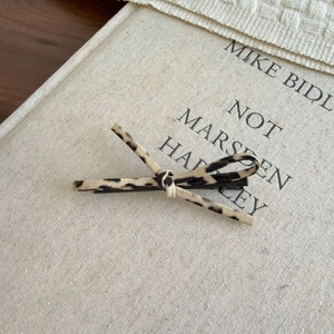 Elegant leopard print bow hair clip on minimalist beige linen book background