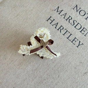 Detail view of pearl hair claw with brown silk bow and golden heart ornament