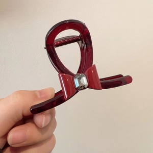 Detail of burgundy resin hair claw clip with bow decoration and crystal inlay