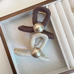 Detailed view of knitted hair claws with golden pearl beads in a wooden jewelry box