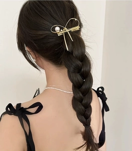 Vue détaillée d'une pince à cheveux dorée avec perle sur une coiffure tressée noire