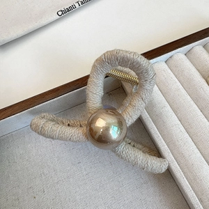 Close-up of a woven cream pearl hair claw clip inside a gray fabric jewelry box