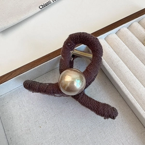 Close-up of brown knit shark hair clip with a large gold bead detail on velvet