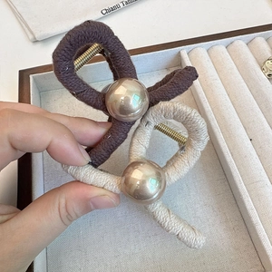 Detail of knitted hair claw clip with large pearl accent in coffee brown and beige tones