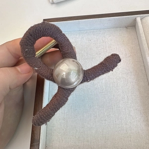 Close-up of a brown knit hair claw clip featuring a metallic silver pearl and gold spring
