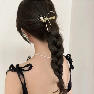 Barrette à cheveux dorée en forme de nœud avec perle portée sur une tresse