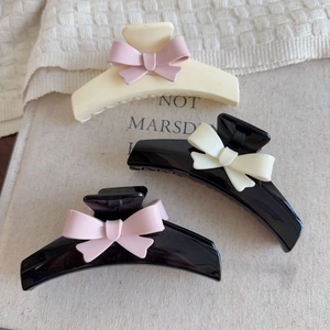 Detailed view of large bow hair claws in cream and black colors on soft fabric