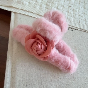 Détail d'une pince à cheveux en peluche rose avec fleur de camélia sur tissu doux