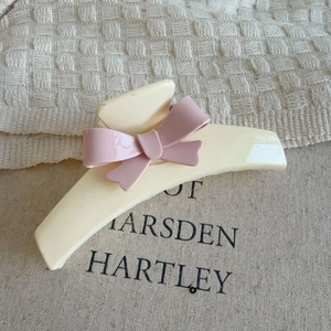 Elegant cream white hair claw clip with a pink bow accent on a soft fabric background