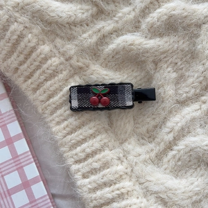 Macro view of checkered fabric hair clip with 3D cherry ornament on a knit background