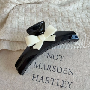 Black large hair claw clip with cream bow decoration on soft textured background