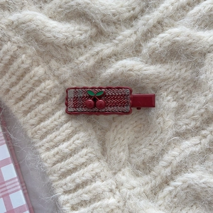 Detail of red cherry hair clip with plaid fabric on minimalist white knit sweater background