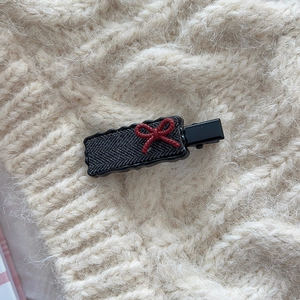 Detail view of retro plaid hair clip with red bow on a textured knit background