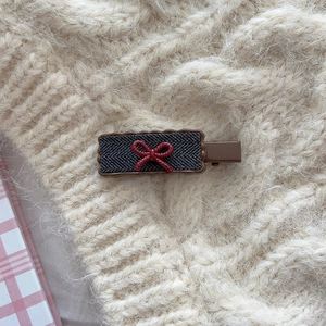 Detail of retro checkered hair clip featuring herringbone fabric and red bow accent