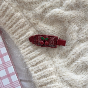 Detail of red plaid cherry hair clip on knit fabric showing retro design textures
