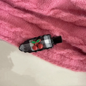 Close-up of a checkered fabric hair clip featuring red cherry and green leaf accents