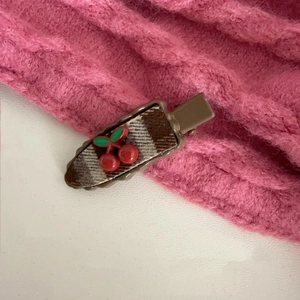 Close-up of a brown plaid hair clip with cute red cherry detail on pink fabric