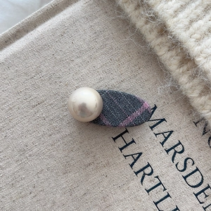 Nahaufnahme einer Haarspange mit marineblauem Karostoff und großer Perle auf künstlerischem Buch