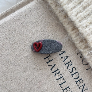 Detail der Haarspange mit lila Karomuster und einem roten 3D-Herz-Akzent auf Stoff