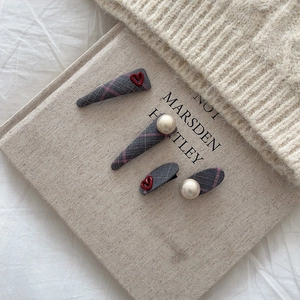 Vierteiliges graues Karo-Haarclip-Set mit roten Herzen und Perlen auf einem Buch