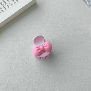 Mini pince à cheveux nœud rose pastel en plastique mat sur fond blanc texturé