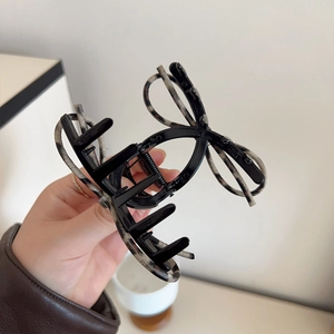 Detail of a large bow-shaped hair claw clip in black and marbled texture held by hand