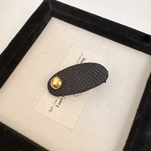 Elegant black woven hair clip with gold rivet on artistic background, minimalist design