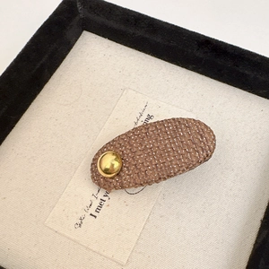 Detail of a brown woven hair clip with a stylish golden metal button on white card