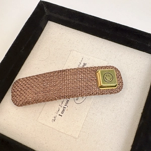 Close-up of brown woven hair claw clip featuring a golden square smiley face charm