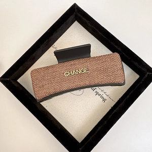Large rectangular woven hair claw clip with golden Change letter logo in champagne brown