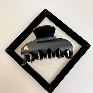 Detail of matte black claw clip featuring a small golden button on a white background