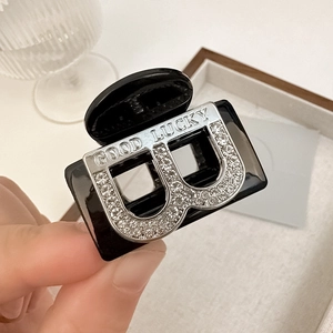 Gros plan sur pince à cheveux noire avec lettres B en cristal et gravure argentée