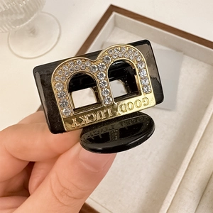 Détail macro d'une pince à cheveux en résine noire avec lettre B dorée et strass
