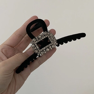 Detail of black velvet hair claw clip with rectangular crystals held by a hand