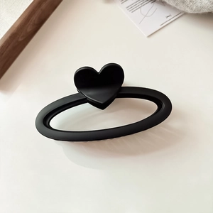 Détail d'une pince à cheveux mate noire en forme de cœur sur un fond minimaliste