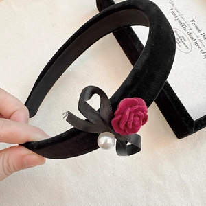 Detail view of velvet headband with deep red rose, black ribbon bow and faux pearl