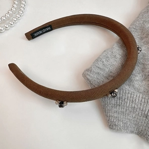 Brown sponge headband with crystal flower embellishments and handmade label on white surface