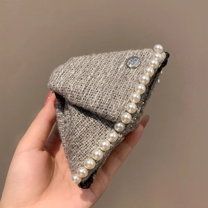 Close-up of houndstooth tweed hair claw with white pearls and Believe metal tag
